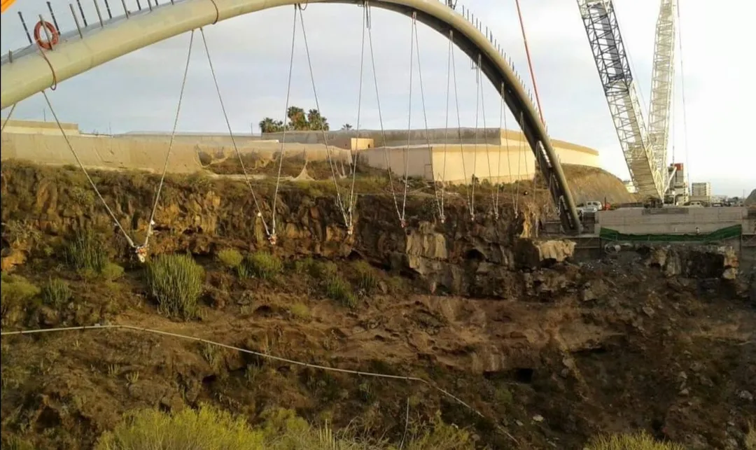 Uno de los arcos suspendido de las grúas sobre el barranco durante el izado